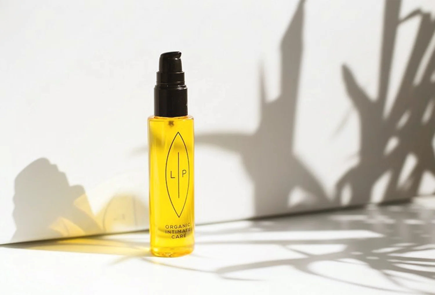 Óleo de limpeza íntima orgânico LIP Intemate Care, frasco pousado em cenário branco com sobras de planta no fundo