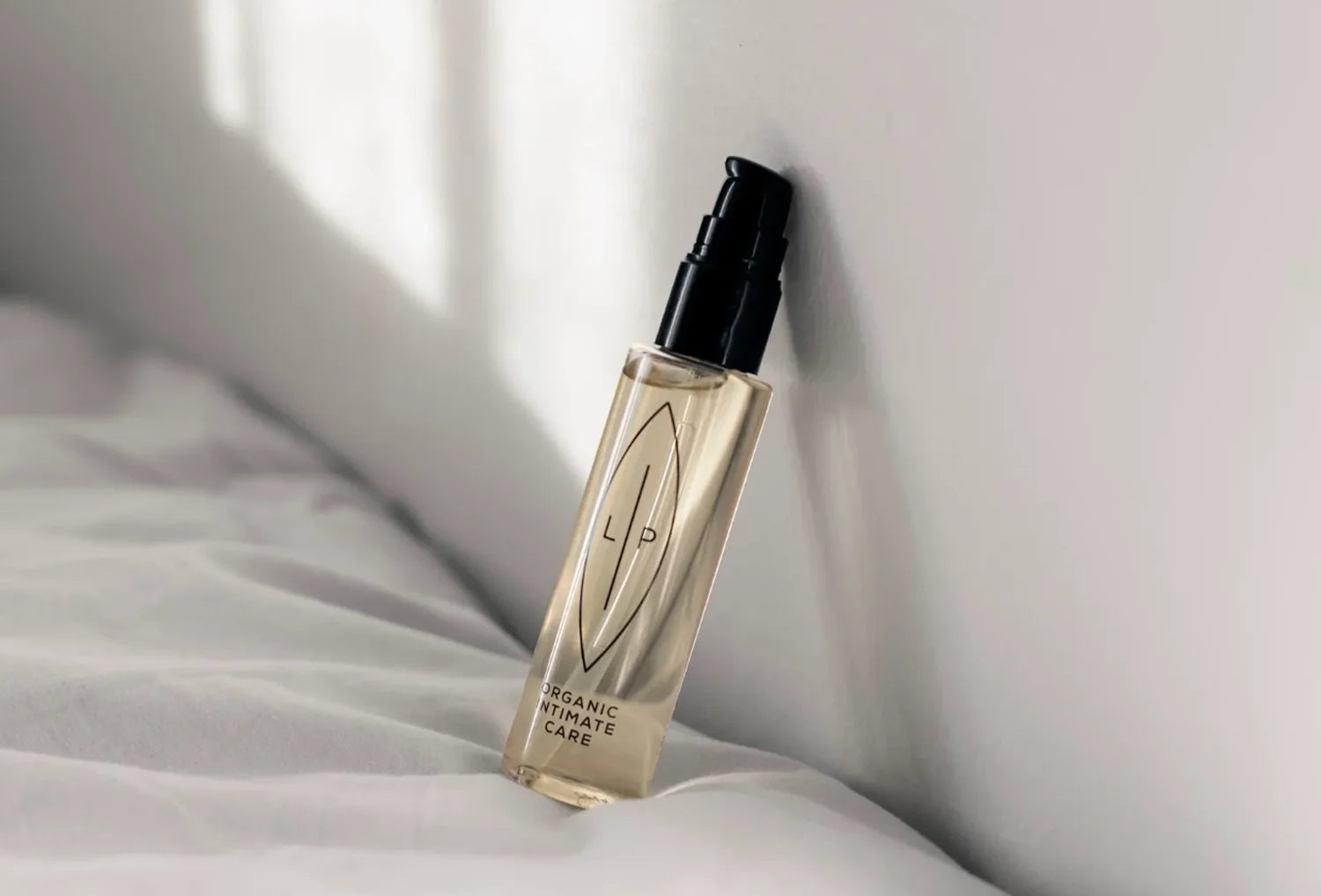 Óleo de limpeza íntima orgânico LIP Intemate Care, frasco pousado numa cama com têxteis brancos.