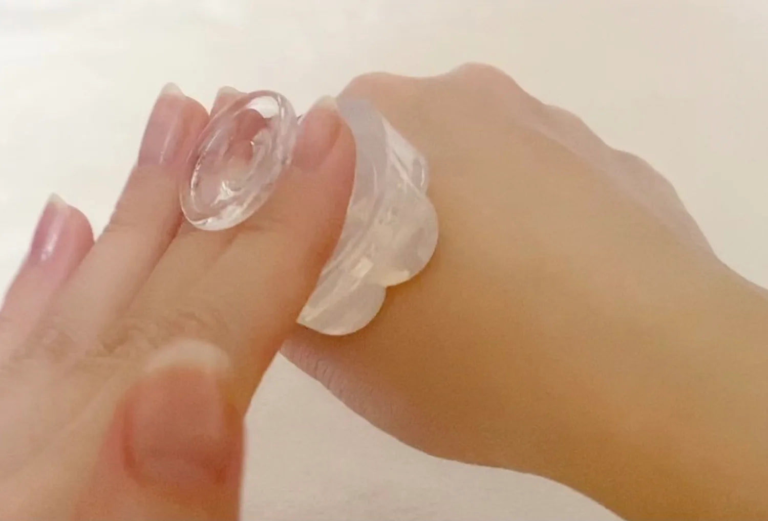 Estimulador clitoriano sem motor Iroha Petit em silicone transparente — segurado na mão a simular o uso na palma da mão