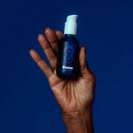 Óleo de massagem Dame Sex Oil num frasco azul — segurado na mão com fundo forte azul