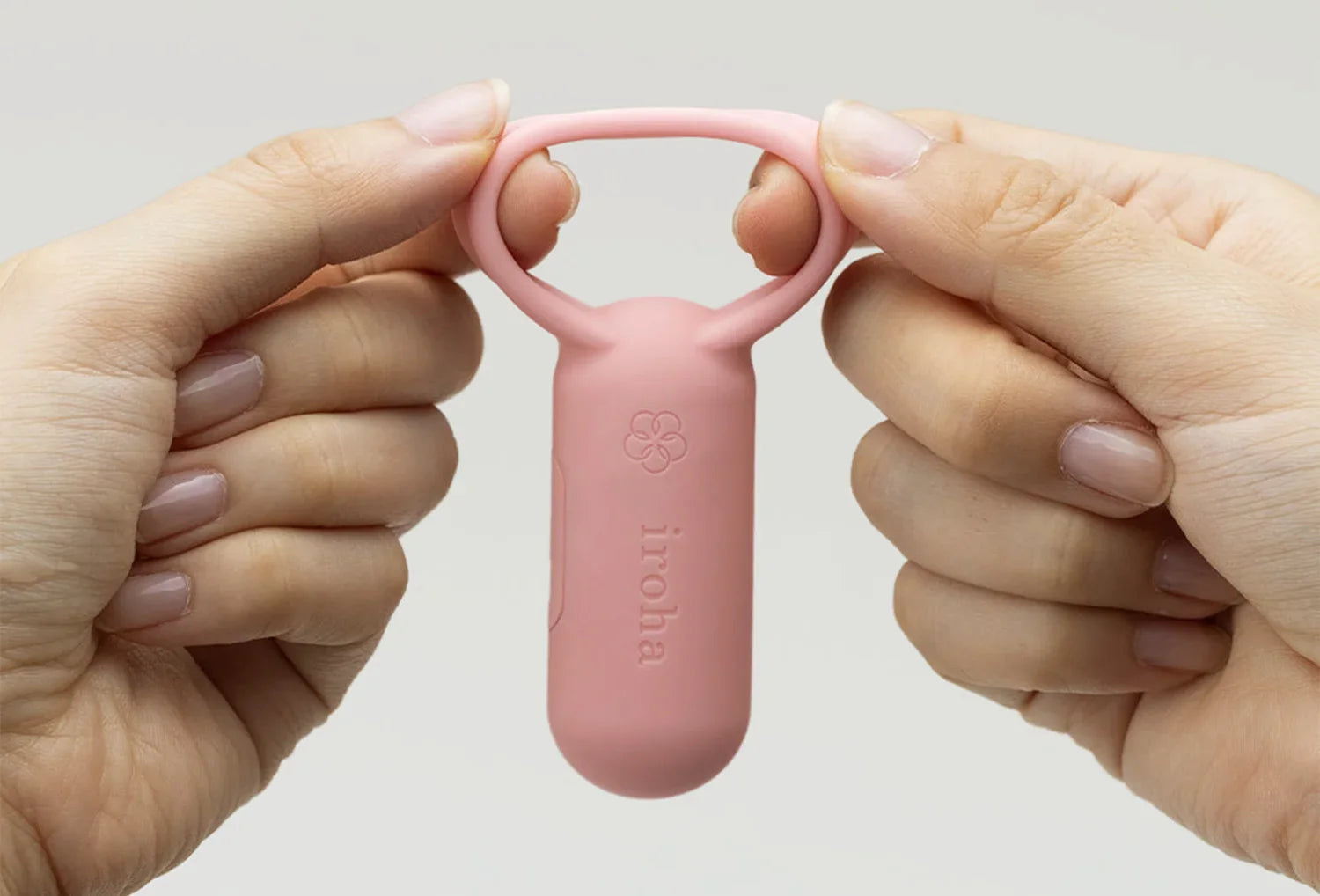 Vibrador clitoriano Iroha SVR em silicone de cor rosa velho — segurado na mão a esticar a alça flexível
