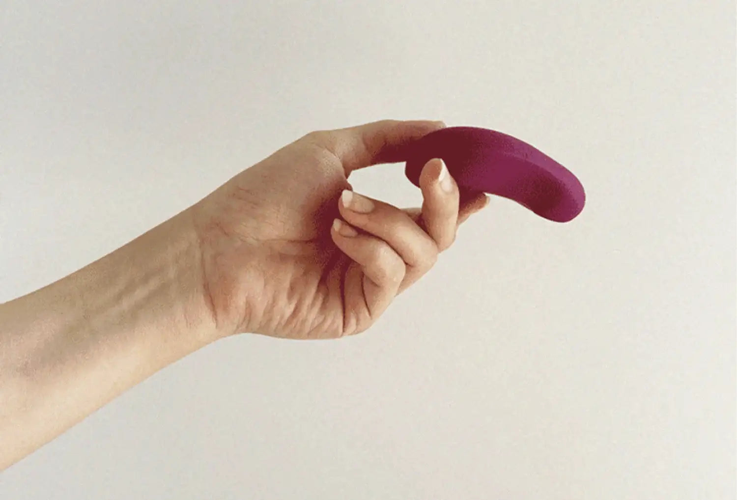 Vibrador clitoriano Dame Pom em silicone de cor ameixa — segurado na mão