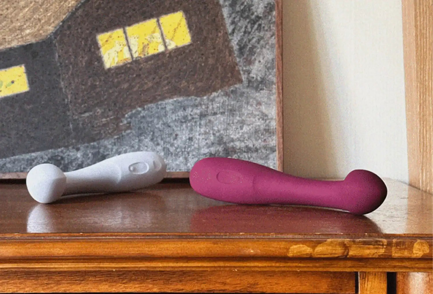 Vibradores de ponto g Dame Arc em silicone de cores lavanda e ameixa pousados em cima de um móvel de madeira escura