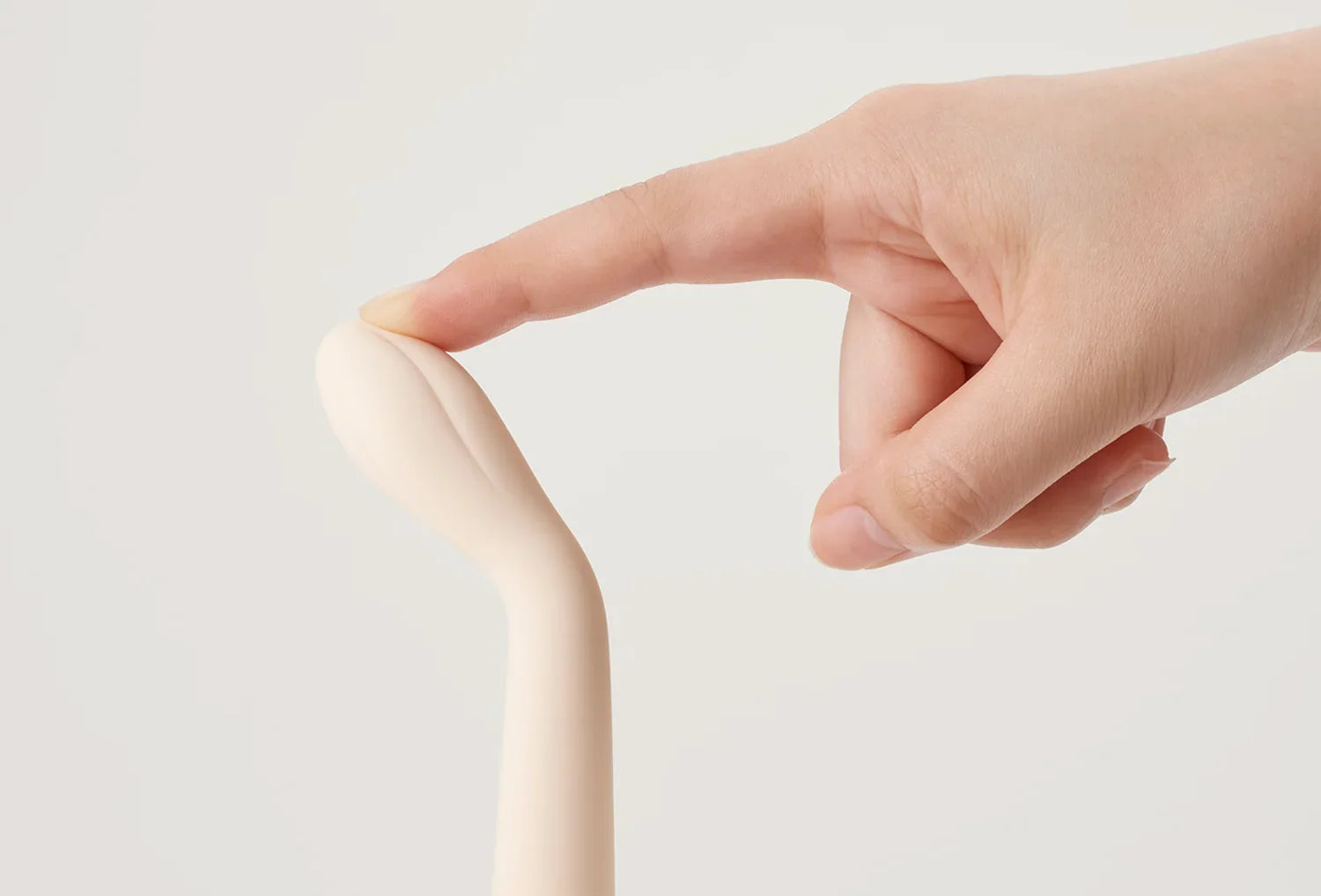 Vibrador clitoriano Iroha Koharu em silicone de cor marfim — com dedo a pressionar a ponta para destacar a flexibilidade